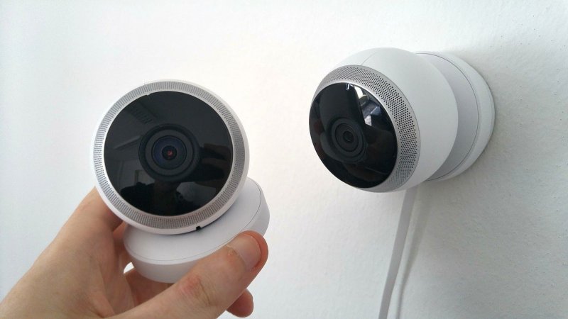 Zwei weiße Überwachungskamera, welche in der Hand gehalten werden und kabelgebunden sind. 