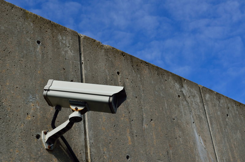 ueberwachungskamera mit arm an einer hohen Betonwand vor blauem himmel